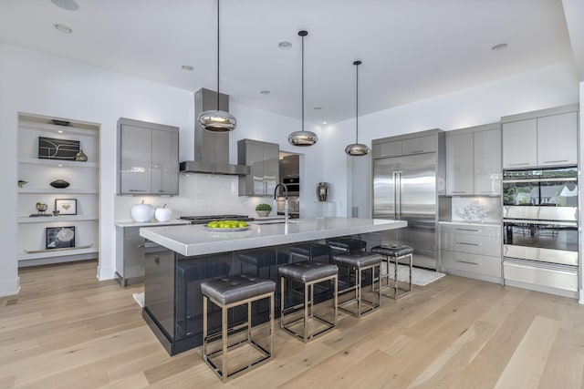 kitchen with gray cabinetry, a kitchen breakfast bar, a large island, stainless steel appliances, and wall chimney range hood