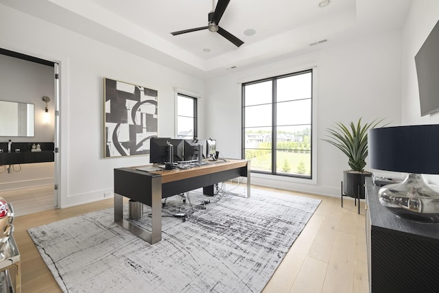 home office featuring hardwood / wood-style floors, a tray ceiling, and ceiling fan