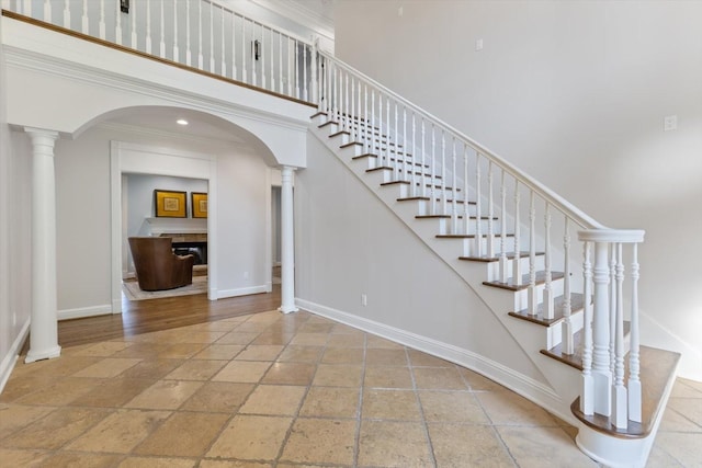 staircase featuring crown molding, decorative columns, and a high ceiling