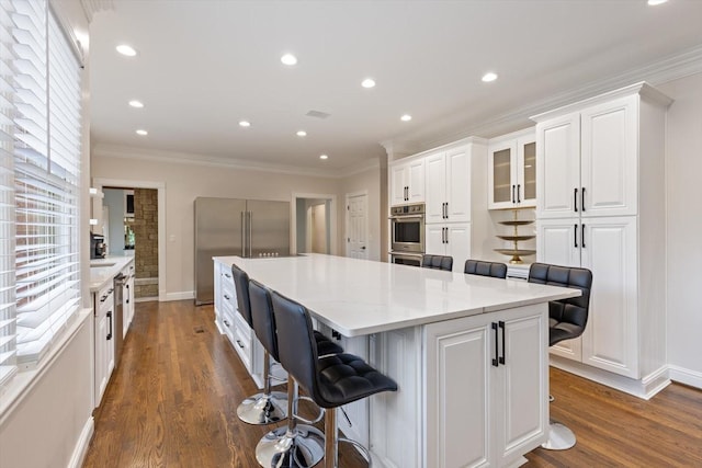 kitchen featuring built in refrigerator, a center island, white cabinets, and a kitchen bar