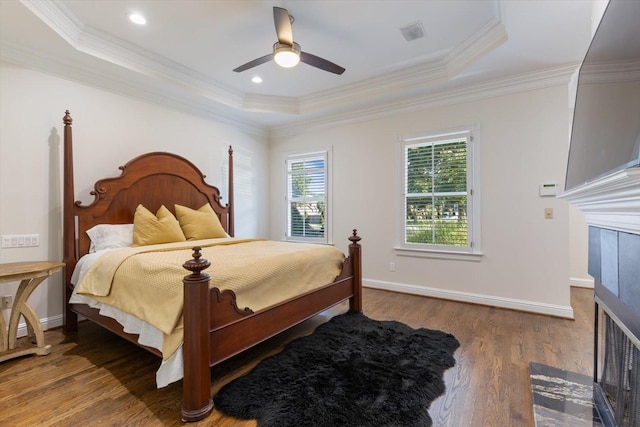 bedroom featuring hardwood / wood-style flooring, a fireplace, a raised ceiling, and crown molding