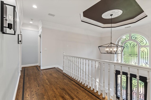 hallway with dark wood-type flooring, ornamental molding, a tray ceiling, and a chandelier