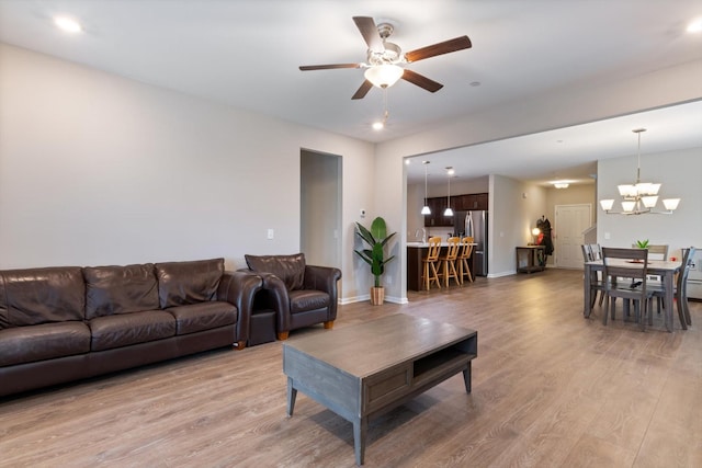 living room with ceiling fan with notable chandelier and light hardwood / wood-style flooring