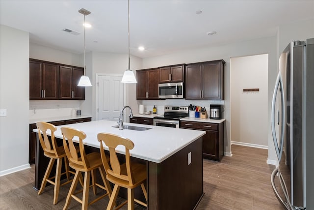 kitchen with pendant lighting, sink, dark brown cabinets, stainless steel appliances, and an island with sink