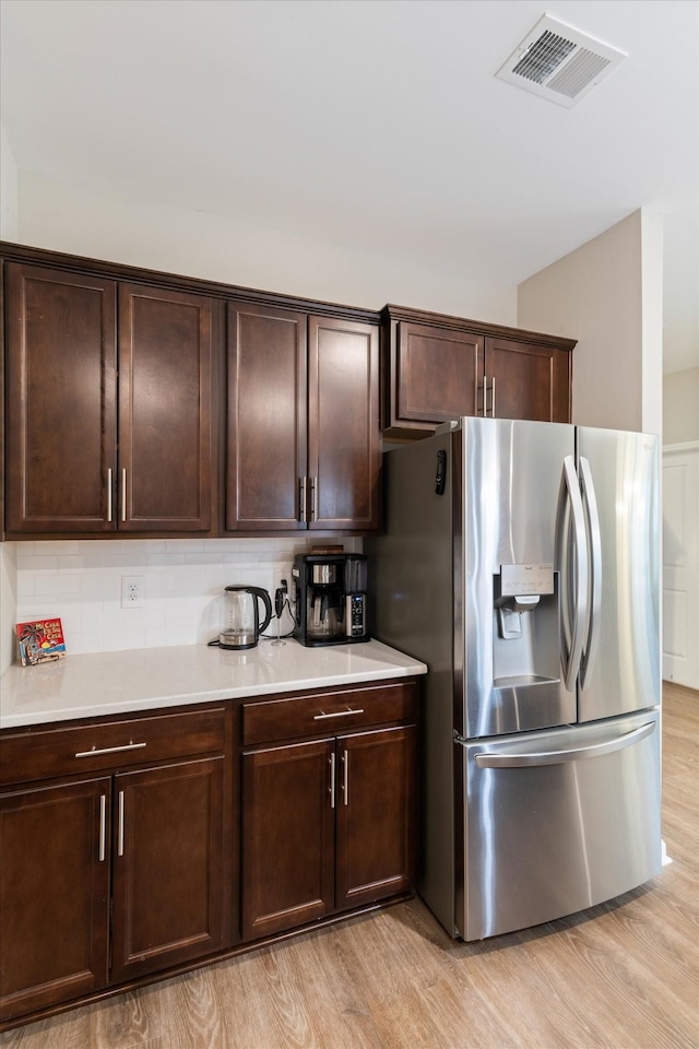 kitchen with dark brown cabinetry, stainless steel fridge with ice dispenser, tasteful backsplash, and light hardwood / wood-style floors