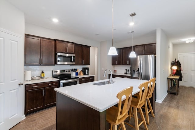 kitchen with hardwood / wood-style floors, sink, hanging light fixtures, a kitchen island with sink, and stainless steel appliances