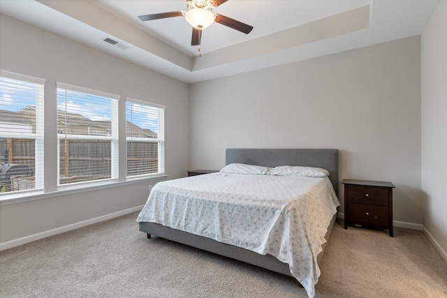 bedroom featuring ceiling fan, a tray ceiling, and light carpet