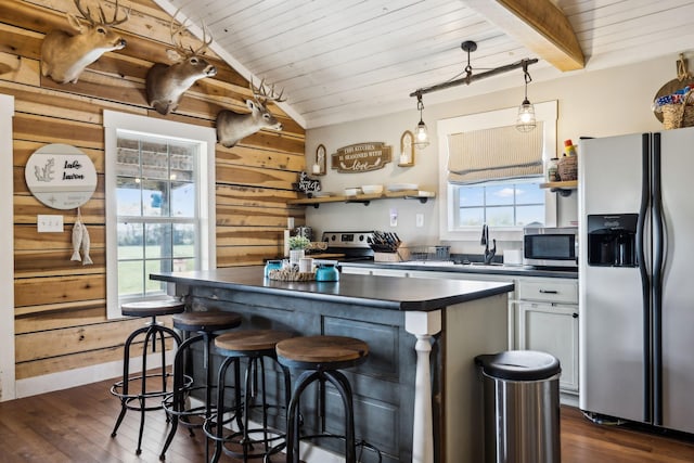 kitchen with appliances with stainless steel finishes, hanging light fixtures, vaulted ceiling with beams, white cabinets, and wood walls