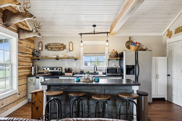 kitchen with a kitchen island, appliances with stainless steel finishes, beamed ceiling, a kitchen breakfast bar, and dark wood-type flooring