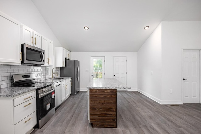 kitchen with white cabinetry, stainless steel appliances, light stone counters, a kitchen island, and vaulted ceiling