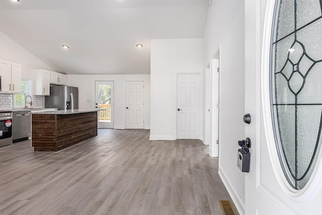 kitchen featuring a center island, light wood-type flooring, white cabinets, stainless steel appliances, and backsplash