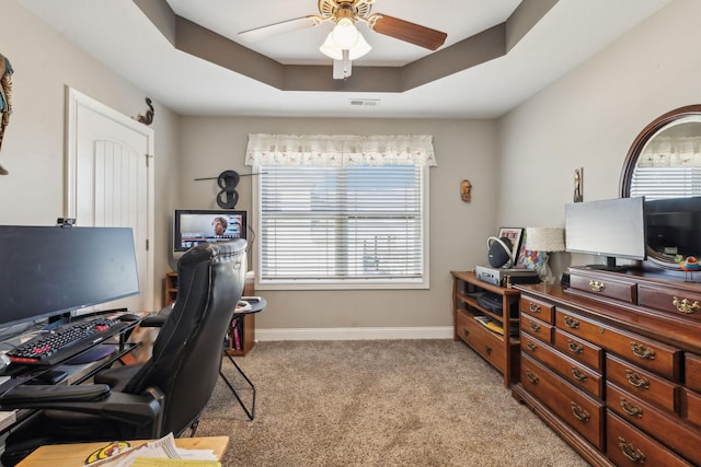 carpeted office space featuring ceiling fan and a tray ceiling