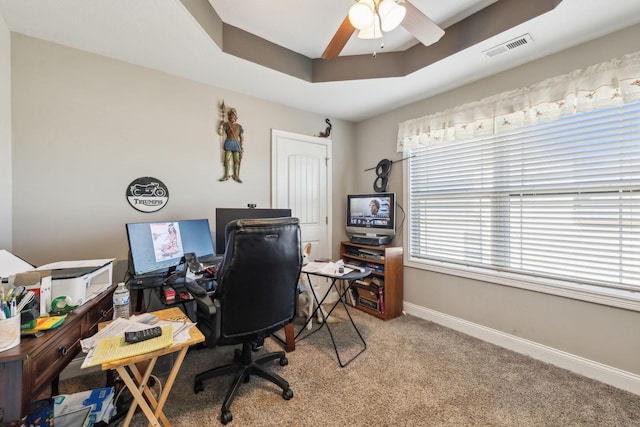 carpeted office featuring a raised ceiling and ceiling fan