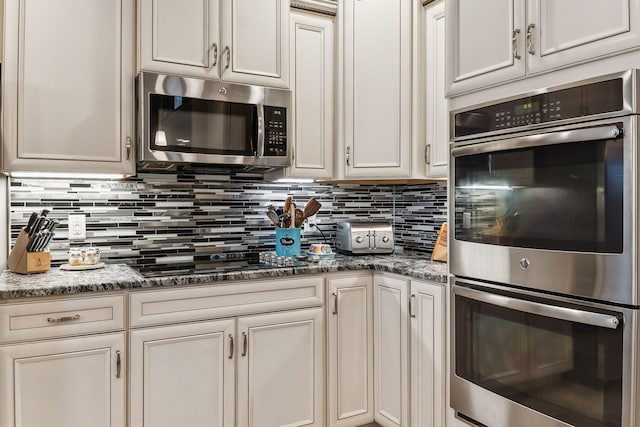 kitchen with stainless steel appliances, decorative backsplash, and dark stone counters