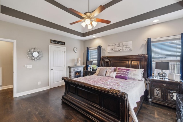 bedroom with ceiling fan, a tray ceiling, and dark hardwood / wood-style flooring