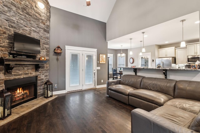 living room with dark hardwood / wood-style flooring, high vaulted ceiling, and a stone fireplace