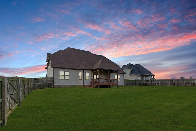 back house at dusk featuring a wooden deck and a yard