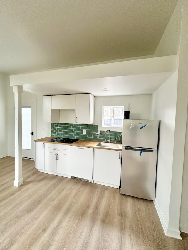 kitchen with sink, white cabinets, stainless steel fridge, decorative backsplash, and light hardwood / wood-style flooring