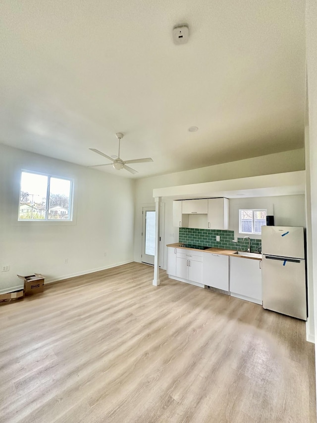 kitchen featuring white cabinetry, backsplash, white fridge, a healthy amount of sunlight, and light wood-type flooring