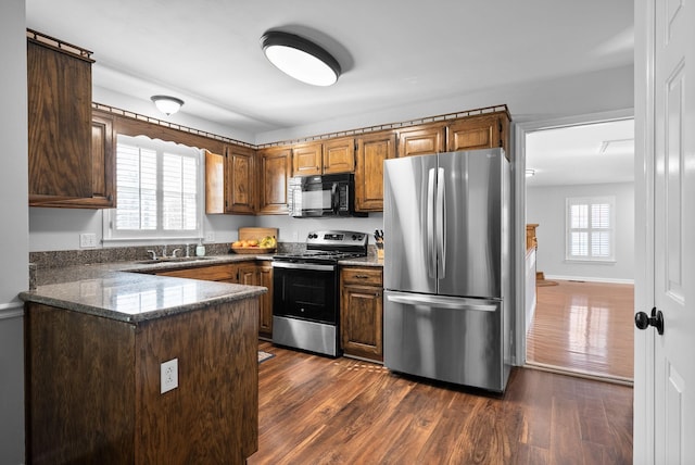 kitchen with dark wood-type flooring, appliances with stainless steel finishes, kitchen peninsula, and sink