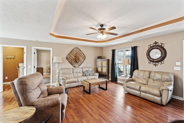 living room with ceiling fan, a tray ceiling, dark wood-type flooring, and a textured ceiling