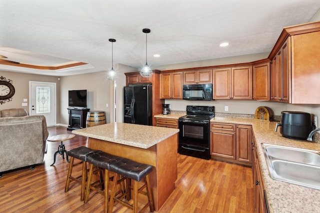 kitchen with a breakfast bar, sink, a tray ceiling, a kitchen island, and black appliances