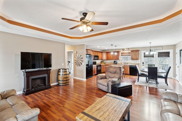 living room with a tray ceiling, sink, ceiling fan with notable chandelier, and light hardwood / wood-style flooring