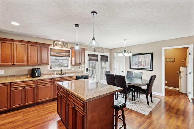 kitchen with sink, dark hardwood / wood-style floors, a center island, light stone counters, and decorative light fixtures