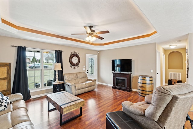 living room featuring dark hardwood / wood-style floors, a textured ceiling, ceiling fan, and a tray ceiling