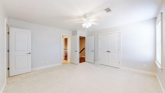 unfurnished bedroom featuring light colored carpet, ensuite bathroom, a closet, and multiple windows