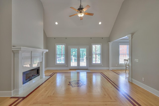 unfurnished living room with decorative columns, high vaulted ceiling, light parquet floors, and ceiling fan