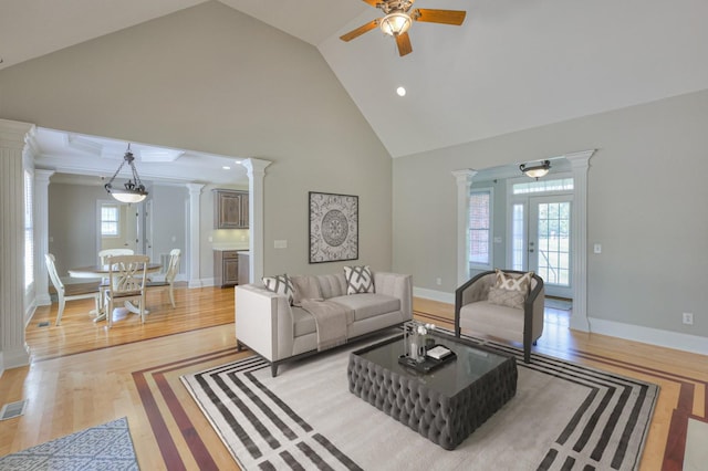 living room featuring high vaulted ceiling, decorative columns, ceiling fan, and light wood-type flooring