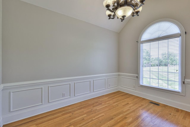 spare room featuring a notable chandelier, vaulted ceiling, and light hardwood / wood-style floors