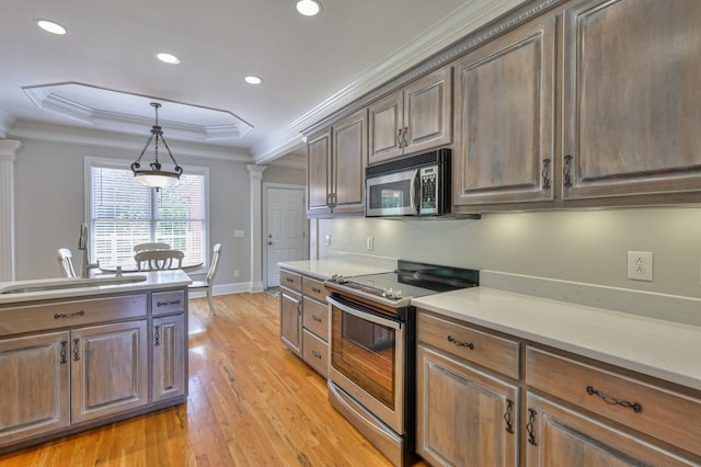 kitchen featuring appliances with stainless steel finishes, decorative columns, sink, light hardwood / wood-style floors, and a raised ceiling