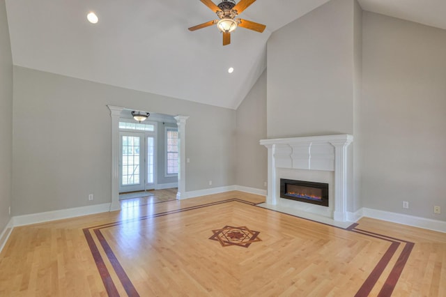 unfurnished living room with high vaulted ceiling, decorative columns, ceiling fan, and light wood-type flooring