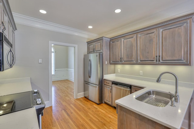 kitchen featuring sink, light stone counters, light hardwood / wood-style flooring, ornamental molding, and stainless steel appliances