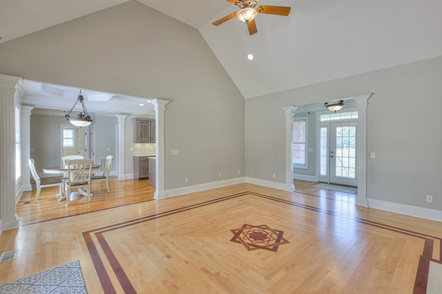 unfurnished living room with ceiling fan, light hardwood / wood-style floors, high vaulted ceiling, and ornate columns