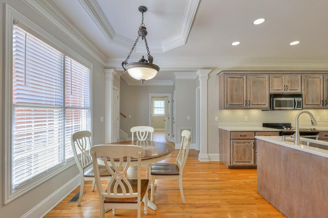 kitchen featuring ornamental molding, stainless steel appliances, decorative columns, and light wood-type flooring