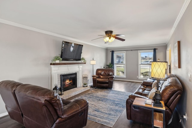 living room with a brick fireplace, crown molding, dark wood-type flooring, and ceiling fan