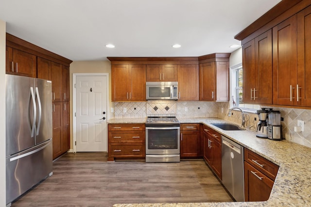 kitchen featuring sink, tasteful backsplash, wood-type flooring, appliances with stainless steel finishes, and light stone countertops