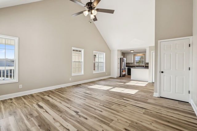 unfurnished living room featuring high vaulted ceiling, light wood-style flooring, and baseboards