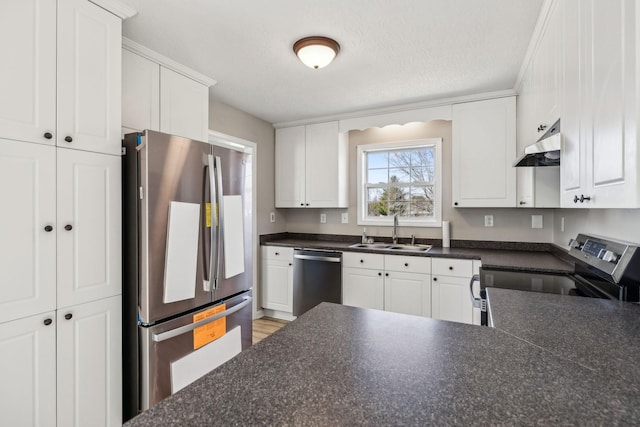 kitchen with dark countertops, appliances with stainless steel finishes, white cabinetry, a sink, and under cabinet range hood