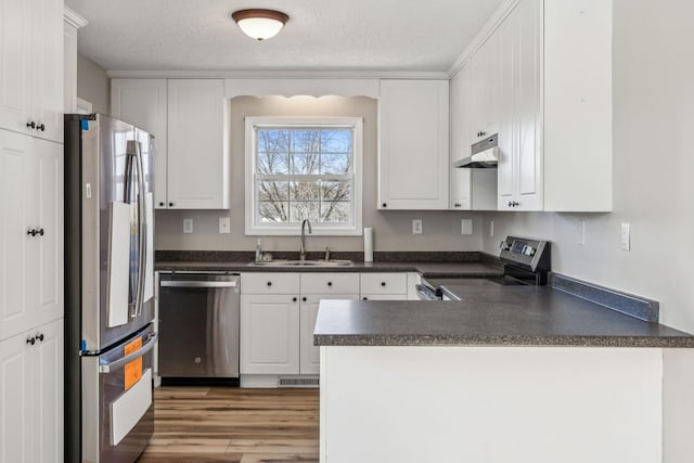 kitchen with dark countertops, appliances with stainless steel finishes, a sink, a peninsula, and exhaust hood