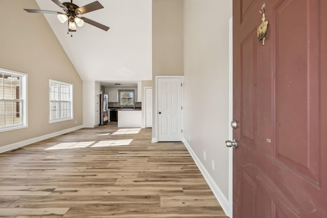 unfurnished living room with light wood-style flooring, high vaulted ceiling, ceiling fan, and baseboards