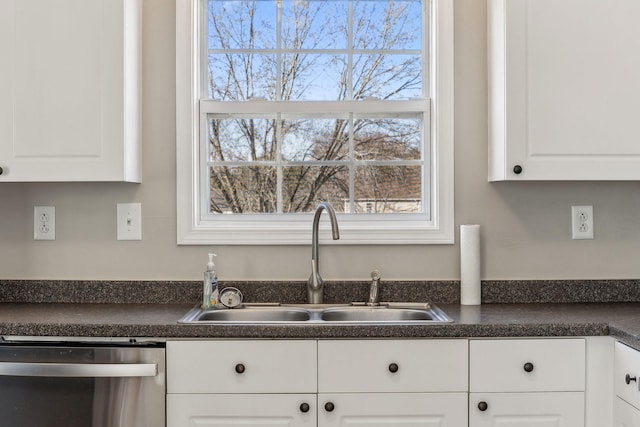 kitchen with dark countertops, white cabinetry, dishwasher, and a sink