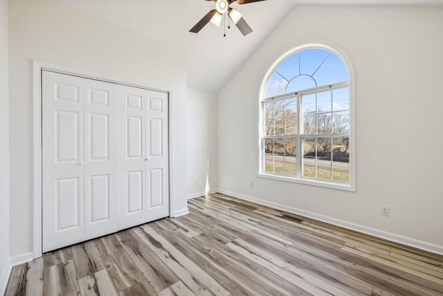 unfurnished bedroom with lofted ceiling, a closet, multiple windows, and wood finished floors