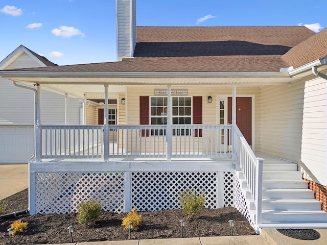 view of exterior entry featuring covered porch, a shingled roof, and a chimney