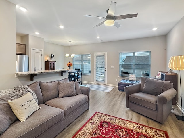 living room with ceiling fan with notable chandelier, a wealth of natural light, and light hardwood / wood-style floors