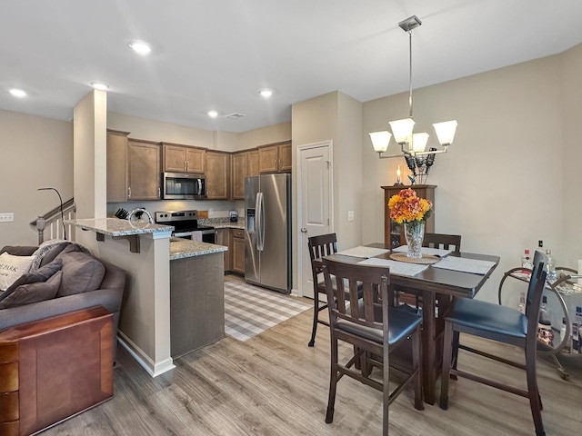 kitchen with hanging light fixtures, stainless steel appliances, light stone countertops, kitchen peninsula, and light wood-type flooring