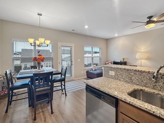 kitchen featuring sink, light stone counters, light hardwood / wood-style floors, decorative light fixtures, and stainless steel dishwasher